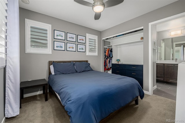 carpeted bedroom featuring a closet, ceiling fan, ensuite bath, and baseboards