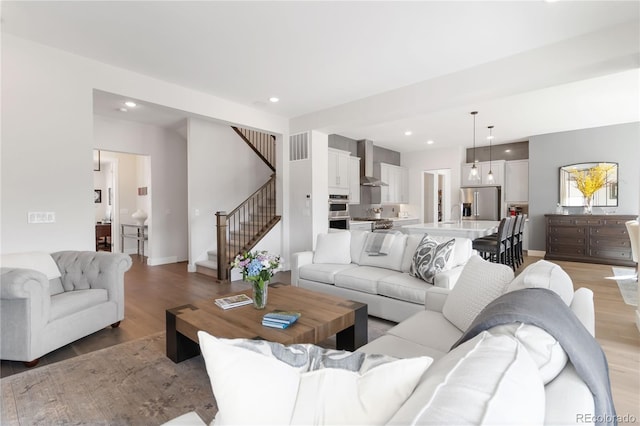 living area featuring recessed lighting, visible vents, light wood-style flooring, and stairs