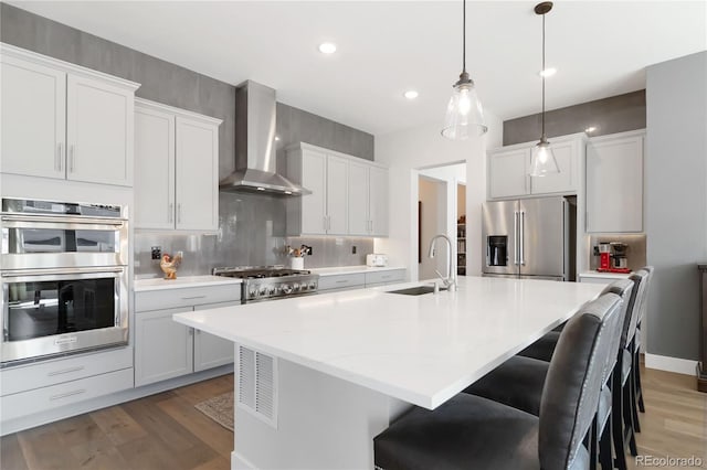 kitchen featuring a sink, wall chimney range hood, appliances with stainless steel finishes, decorative backsplash, and light wood finished floors
