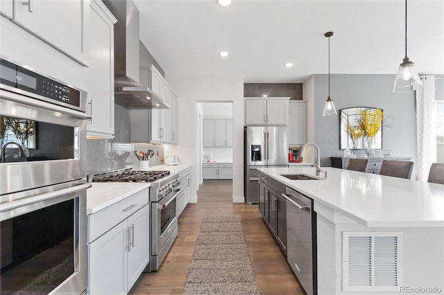 kitchen featuring tasteful backsplash, wall chimney exhaust hood, appliances with stainless steel finishes, light countertops, and a sink