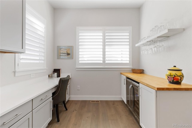 kitchen featuring wine cooler, built in desk, butcher block counters, light wood-type flooring, and baseboards
