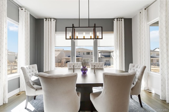 dining room with a notable chandelier, baseboards, wood finished floors, and a healthy amount of sunlight