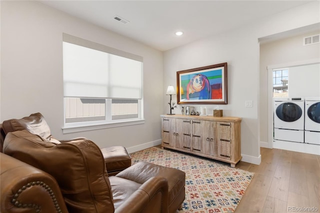 living area with washer and clothes dryer, light wood-type flooring, visible vents, and baseboards