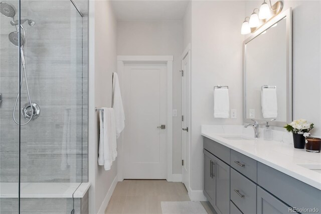bathroom with double vanity, baseboards, a tile shower, and a sink