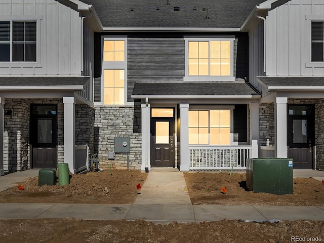 entrance to property featuring board and batten siding, stone siding, and a shingled roof