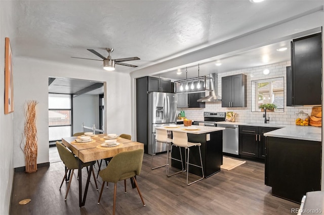 kitchen featuring wall chimney exhaust hood, a kitchen island, appliances with stainless steel finishes, and a healthy amount of sunlight