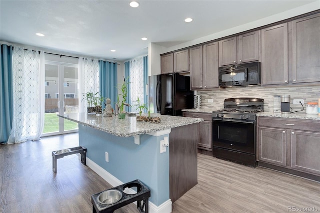 kitchen with a kitchen island with sink, black appliances, light stone counters, and light wood-type flooring