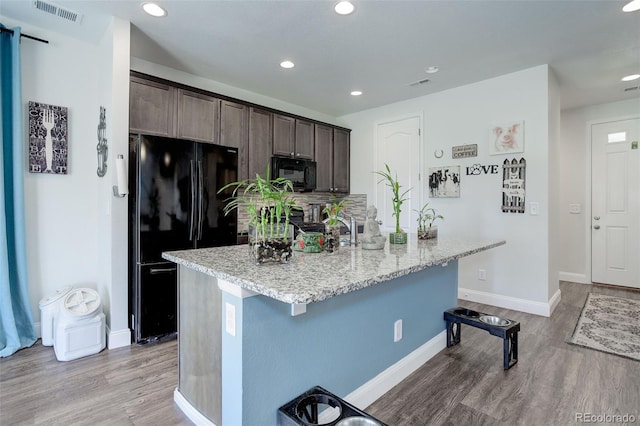 kitchen with dark brown cabinets, light hardwood / wood-style floors, a kitchen island with sink, and black appliances