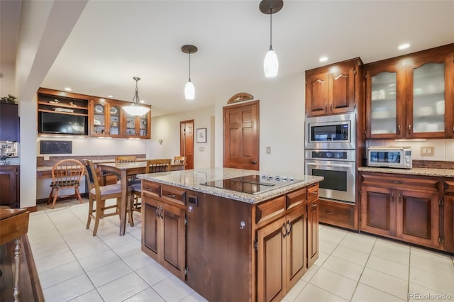 kitchen with light tile patterned floors, a kitchen island, appliances with stainless steel finishes, decorative light fixtures, and light stone countertops