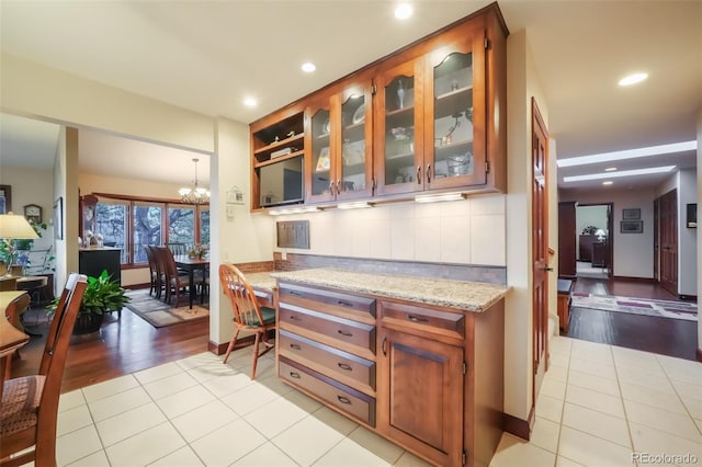 kitchen featuring light tile patterned floors, tasteful backsplash, glass insert cabinets, a notable chandelier, and recessed lighting