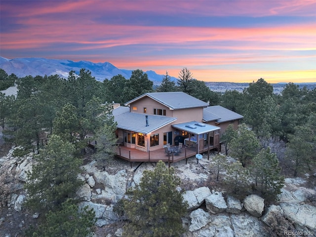 back of house at dusk with a deck with mountain view and a tiled roof