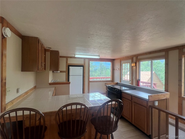 95 Appleby St, Bailey, CO 80421 - kitchen featuring freestanding refrigerator, tile counters, a peninsula, a textured ceiling, and brown cabinets