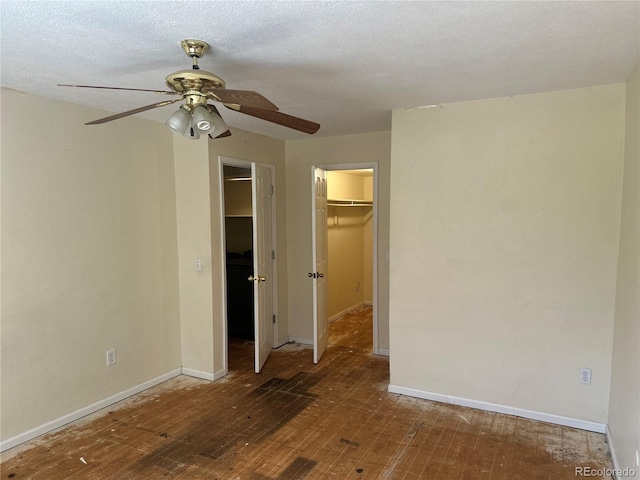 unfurnished bedroom featuring baseboards, a ceiling fan, wood finished floors, a closet, and a walk in closet