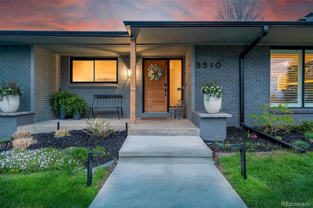 exterior entry at dusk featuring a porch and brick siding