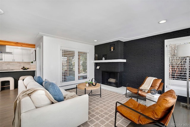 living room featuring a fireplace, recessed lighting, baseboard heating, brick wall, and wood finished floors