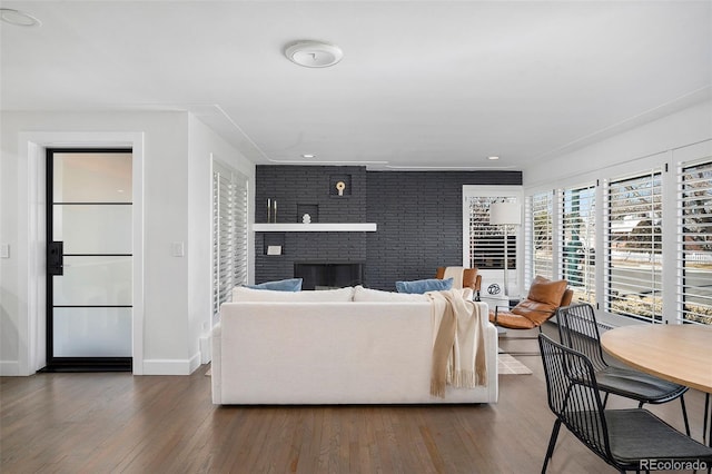 living room with brick wall, a brick fireplace, wood finished floors, and baseboards