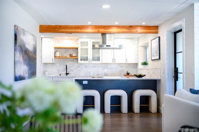 kitchen with tasteful backsplash, beam ceiling, white cabinetry, and wall chimney exhaust hood