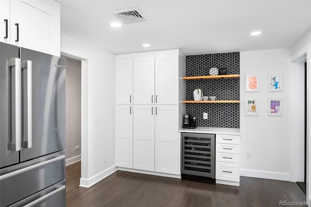 bar featuring beverage cooler, visible vents, dark wood-type flooring, freestanding refrigerator, and a bar