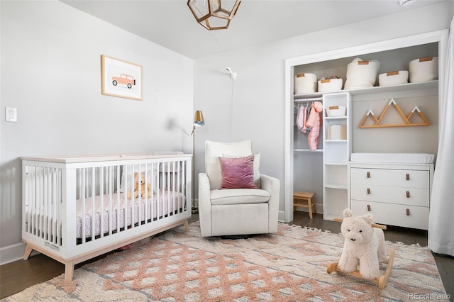 bedroom with a nursery area, a closet, and wood finished floors