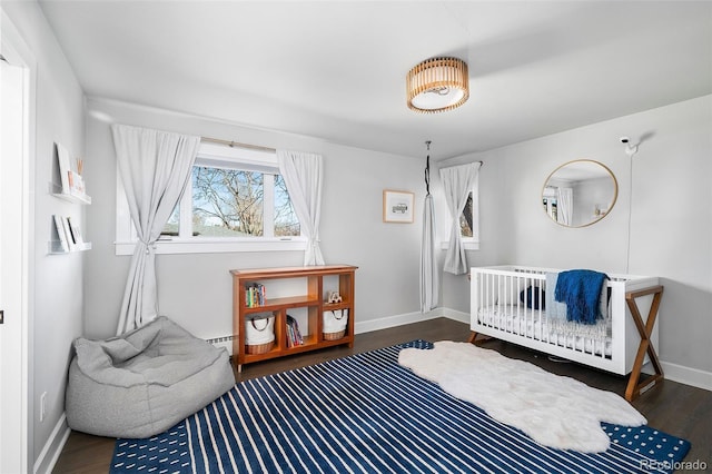 bedroom with baseboards, a crib, baseboard heating, and wood finished floors