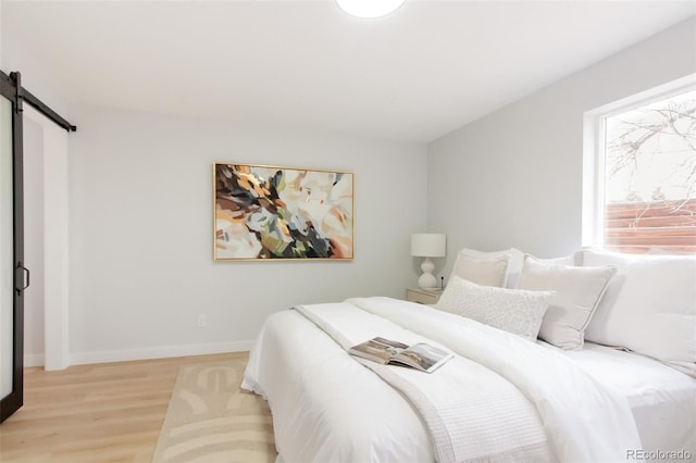 bedroom with baseboards, a barn door, and light wood-style floors