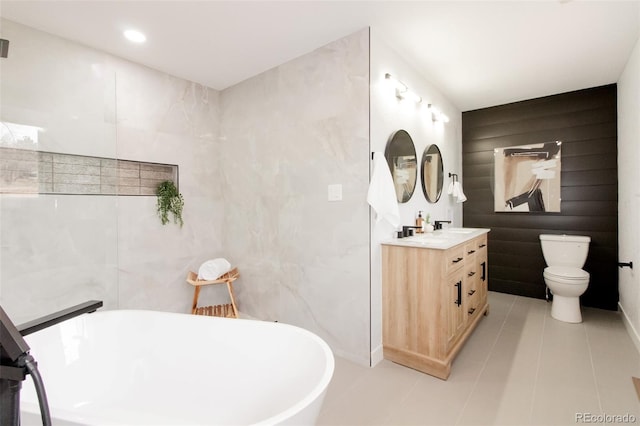 bathroom featuring toilet, a soaking tub, tile patterned flooring, vanity, and tile walls