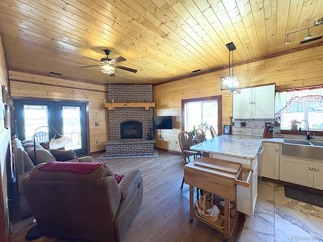 living room with wooden ceiling, ceiling fan, wooden walls, a fireplace, and light wood-style flooring