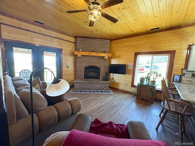 living room with wood finished floors, visible vents, ceiling fan, wooden walls, and wood ceiling
