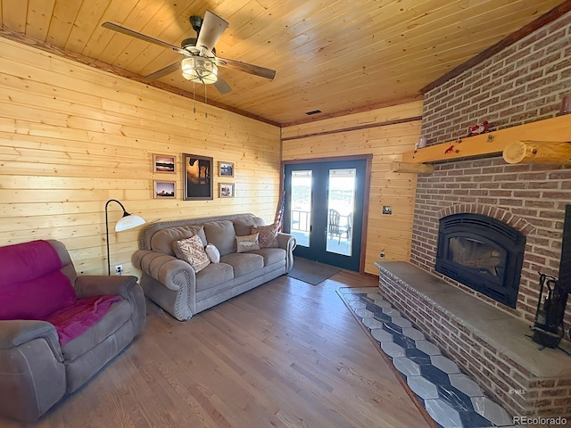living area with a ceiling fan, wooden ceiling, a brick fireplace, wood walls, and wood finished floors