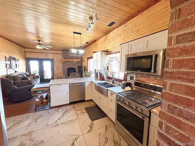 kitchen with a ceiling fan, a sink, open floor plan, appliances with stainless steel finishes, and wooden walls