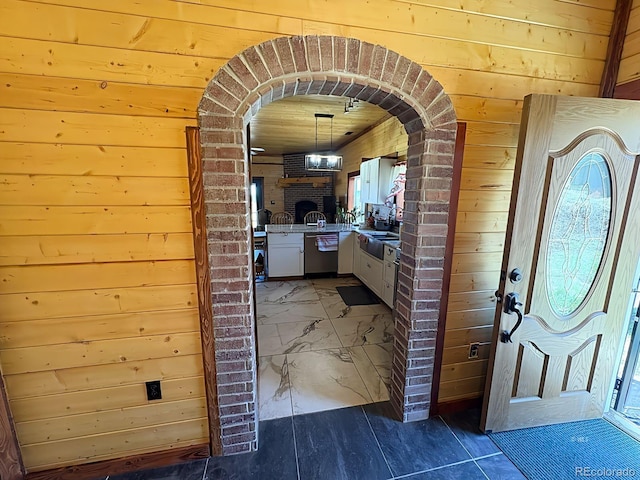 interior space with stainless steel dishwasher, white cabinetry, wood walls, and arched walkways
