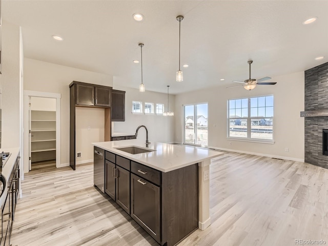 kitchen featuring a tile fireplace, ceiling fan, sink, stainless steel dishwasher, and a center island with sink