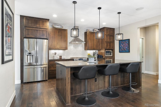1882 W 67th Ave, Denver, CO 80221 - kitchen featuring appliances with stainless steel finishes, dark wood-style floors, wall chimney exhaust hood, tasteful backsplash, and a center island with sink