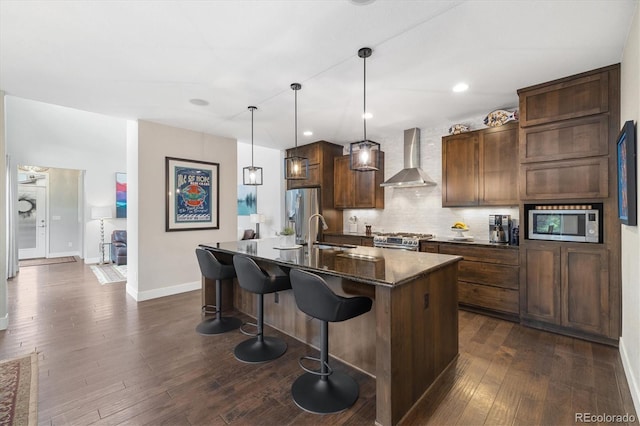 1882 W 67th Ave, Denver, CO 80221 - kitchen with wall chimney exhaust hood, appliances with stainless steel finishes, a kitchen island with sink, backsplash, and dark wood-style flooring