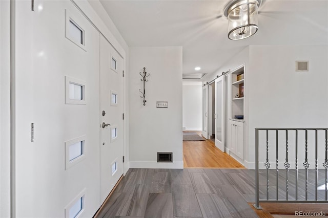 corridor featuring a barn door, wood finished floors, visible vents, and baseboards