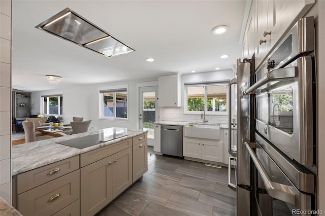 kitchen featuring light stone countertops, a sink, stainless steel appliances, white cabinetry, and backsplash