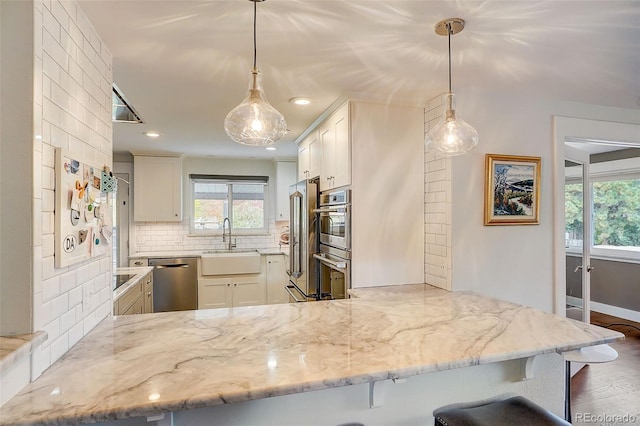 kitchen with a sink, stainless steel appliances, light stone countertops, and backsplash