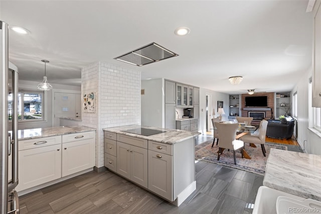 kitchen featuring a brick fireplace, black electric stovetop, light stone countertops, a peninsula, and hanging light fixtures