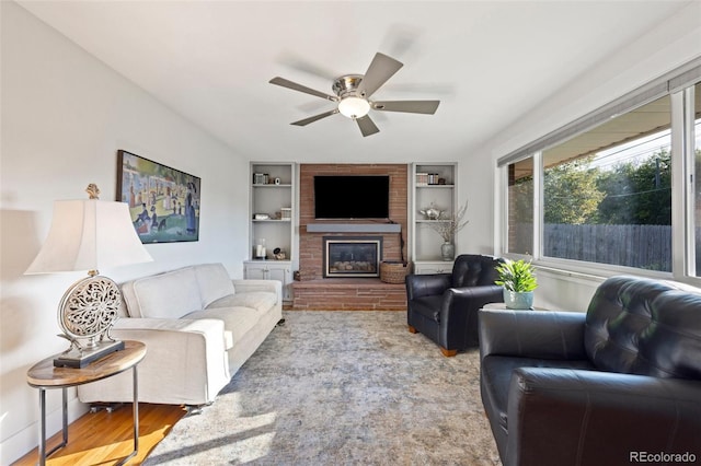 living room featuring ceiling fan, built in shelves, a brick fireplace, and wood finished floors