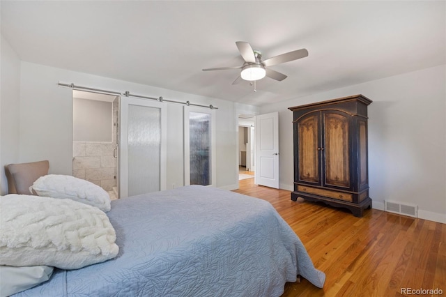 bedroom featuring visible vents, a ceiling fan, a barn door, light wood-style floors, and baseboards