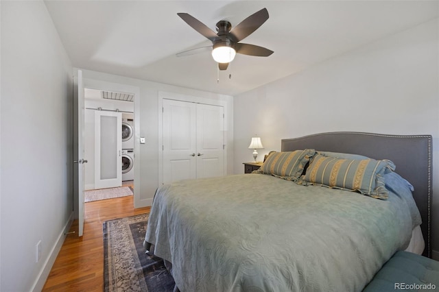 bedroom featuring baseboards, a barn door, stacked washer and clothes dryer, wood finished floors, and a closet