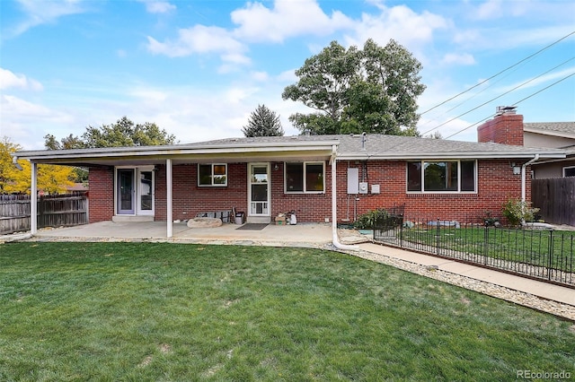 rear view of house featuring brick siding, a lawn, a patio, and fence