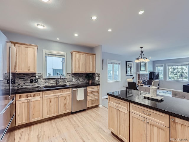 kitchen with light brown cabinets, light wood-type flooring, dishwasher, a tile fireplace, and sink