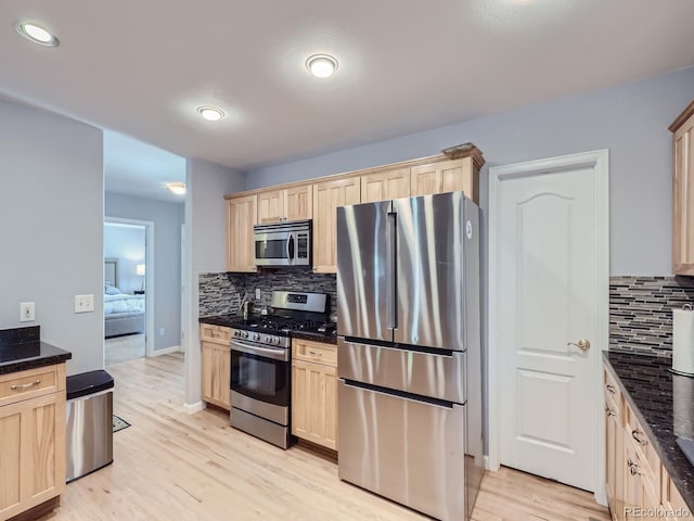 kitchen featuring appliances with stainless steel finishes, light hardwood / wood-style flooring, dark stone countertops, and backsplash