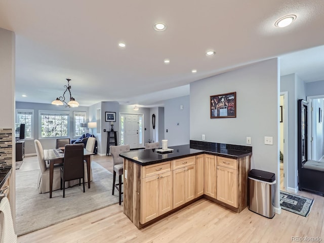 kitchen with light brown cabinets, hanging light fixtures, a kitchen breakfast bar, an inviting chandelier, and light hardwood / wood-style floors