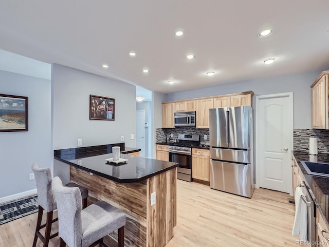 kitchen featuring backsplash, a breakfast bar, appliances with stainless steel finishes, and light wood-type flooring