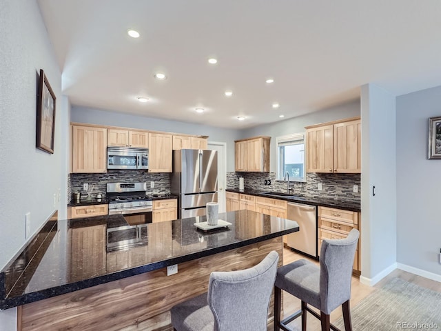 kitchen featuring light hardwood / wood-style flooring, stainless steel appliances, sink, a breakfast bar, and tasteful backsplash