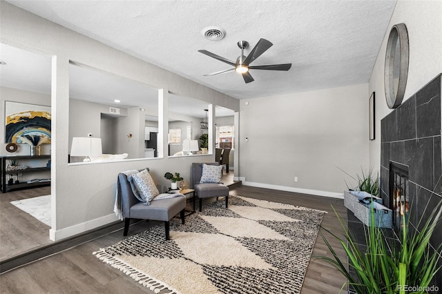 living area with baseboards, visible vents, a tile fireplace, wood finished floors, and a textured ceiling