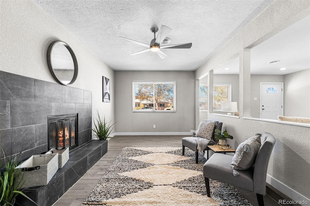 sitting room with a fireplace, a ceiling fan, a textured ceiling, wood finished floors, and baseboards