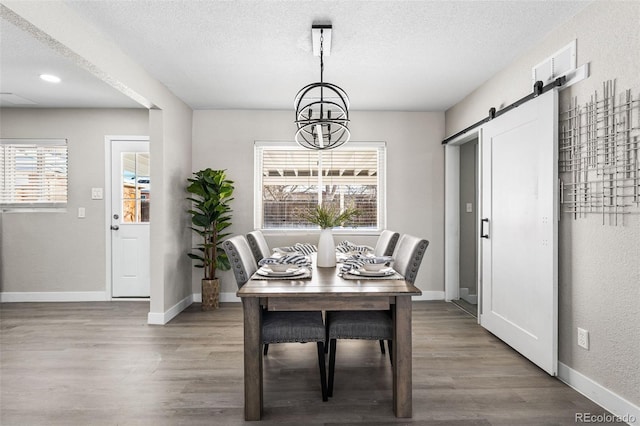 dining room featuring a barn door, a textured ceiling, wood finished floors, a chandelier, and baseboards